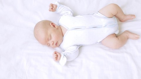 cute little newborn baby boy sleeps in the nursery on a white cotton bed at home