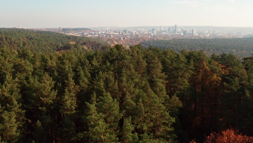 Establishing aerial shot over the forest and river to the Vilnius city center in the background, beautiful autumn nature. Flying forward and zooming out. Royalty-Free Stock Footage #1077737279