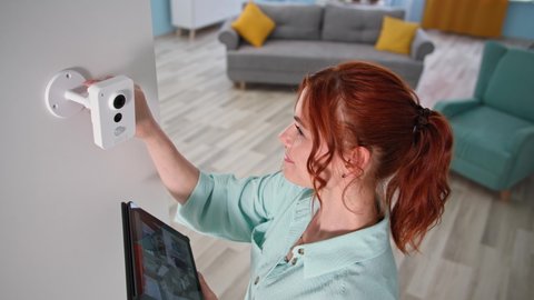 female homeowner controls home video surveillance with tablet indoors, girl checking the camera with gadget in her hands Video de stock