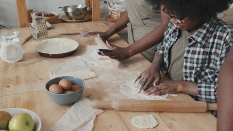 Midsection slowmo of African American family of three making apple pie together at home, rolling out dough on kitchen table