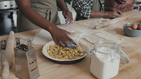 High-angle midsection shot with slowmo of unrecognizable African American woman making delicious apple pie while her husband and son helping her standing together by kitchen table