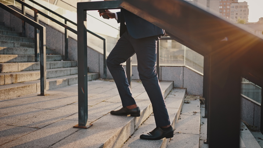 Career ladder concept. close up shot of unrecognizable businessman in formal suit going up on outdoor stairs, slow motion, tracking shot, side view