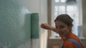 Cheerful woman making wide strip of paint by roller on wall. Joyful girl painting wall in new house. Happy female person doing home repair indoors. House renovation diy concept. - Powered by Shutterstock - Get 15% off with code: PIKWIZARD15