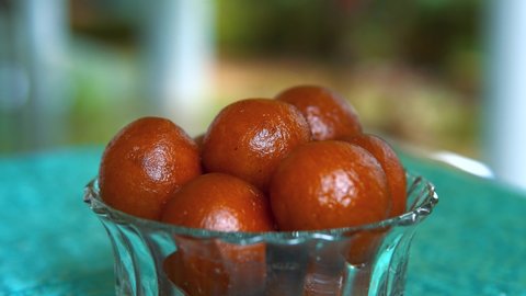sugar syrup pouring on a bowl full of Gulab jamun. Indian dessert dish 