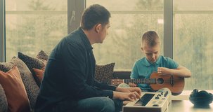 Father and son play guitar and piano at home. Dad teaches child to play musical instruments. Music hobby, Create, learning own songs. SHARE THE LOVE, play our game. 4K video.
