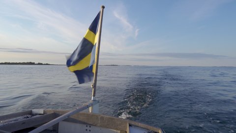Swedish flag waving in the wind at the rear of a boat traveling the sea