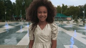 Video of a girl of African appearance who smiles and rejoices against the background of the fountain