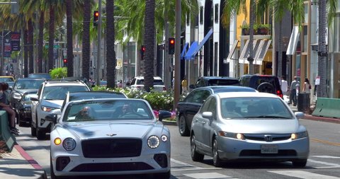 BEVERLY HILLS, LOS ANGELES, CALIFORNIA - JUNE 20, 2021: Luxury cars driving on Rodeo Drive landmark in Beverly Hills, Los Angeles, California, 4K