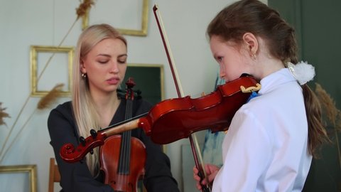 Violin lesson - blonde woman teaching little girl how to hold a violin