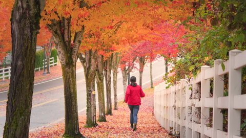 Teenage girl jogging along sidewalk in beautiful autumn foliage while leaves falling from the tree on a windy day