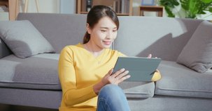 Young Asian woman using digital tablet to watch movie happily while sitting on floor when relax at home