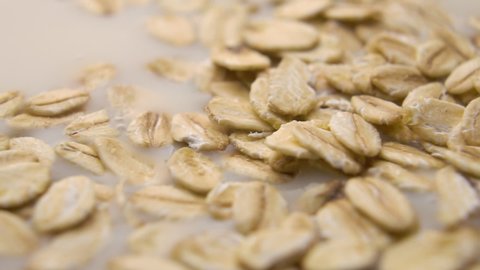 Oat flakes fall into vegetable oat milk. Cooking a healthy nutritious vegetarian breakfast. Macro. Slow motion.