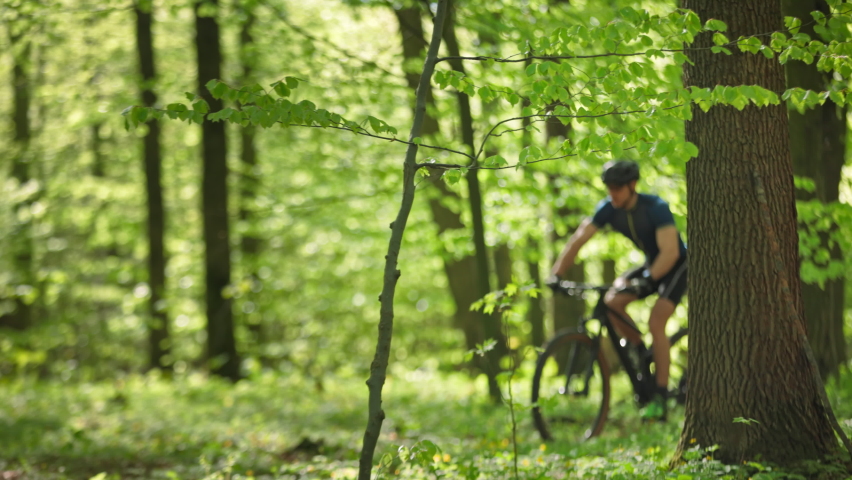 A cyclist quickly passes through a forest road. He is making a quick sprint. He is going around fallen trees. The camera is moving from right to left and follows him. 4K