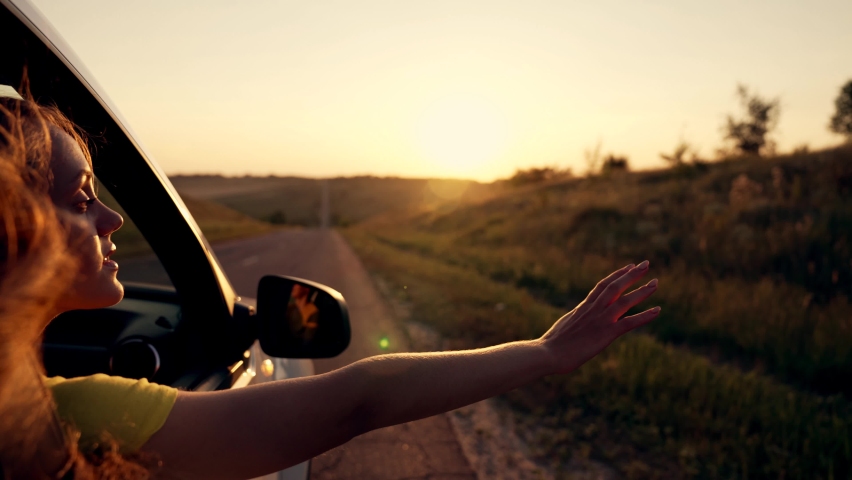 Happy girl in car window. Hair in wind. Girl travels by car. Hand in sun. Windy breeze from car window. Happy girl smiling from car window. Windy breeze in your hair. Hand in the rays of the sun | Shutterstock HD Video #1077778187