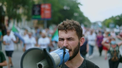 Angry political protester guy with bullhorn marches in protest crowd. Male rebel speaking on demonstration revolt resistance. Strike activist demonstrator man on opposition rally riot with megaphone.