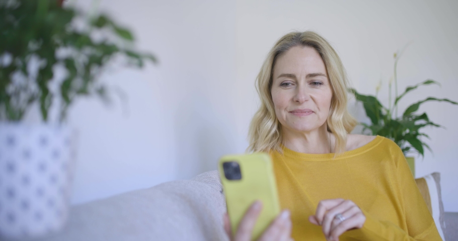 Mature woman sitting on sofa making video call on smartphone