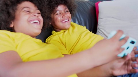 Twin brothers lying on couch watching video on smartphone