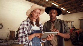 Caucasian female farmer holding digital tablet while mixed race male points around storeroom.