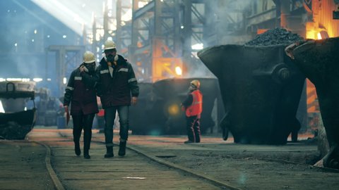 Steel workers are walking along the premises of the factory. Metallurgical factory concept.
