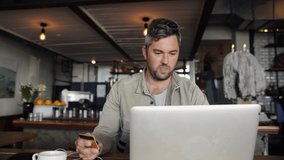 Handsome middle aged man making online payment on laptop holding credit card sitting in cafe.