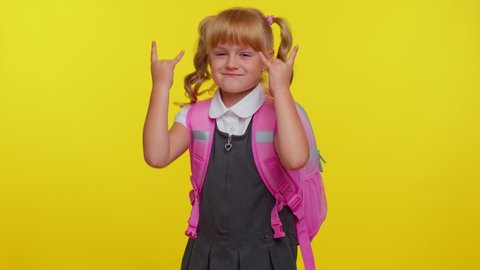Overjoyed delighted funny pupil school girl teenage showing rock n roll gesture by hands, cool sign, shouting yeah with crazy expression, dancing, rejoicing in success on yellow studio background