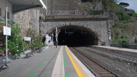 Riomaggiore, Italy - June 11. 2021: Train Station in Riomaggiore, Cinque Terre. Empty Tracks and platform, panning from platform over tracks to view of Mediterranean Sea