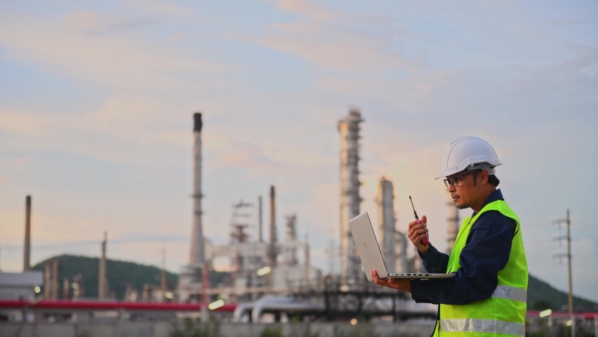 Engineer wearing safety uniform and helmet looking detail notebook on hand and radio communication with oil refinery factory at night time background. Royalty-Free Stock Footage #1077797258