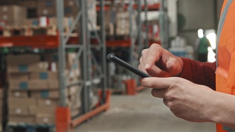 Handheld slowmo mid-section of unrecognizable male worker using mobile phone in warehouse