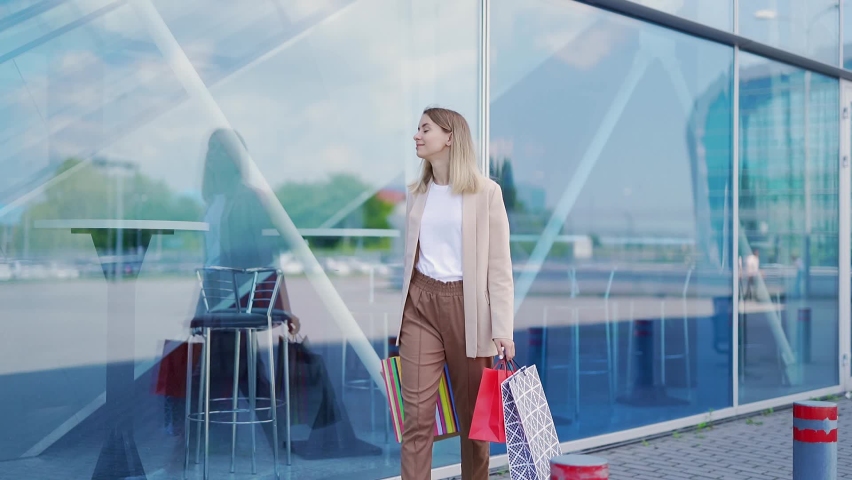happy cheerful young woman goes after shopping with gift paper bags. Satisfied female in outdoor mall. Smiling walks on the background a modern center. portrait tourist sale surpermarket. black friday Royalty-Free Stock Footage #1077799115