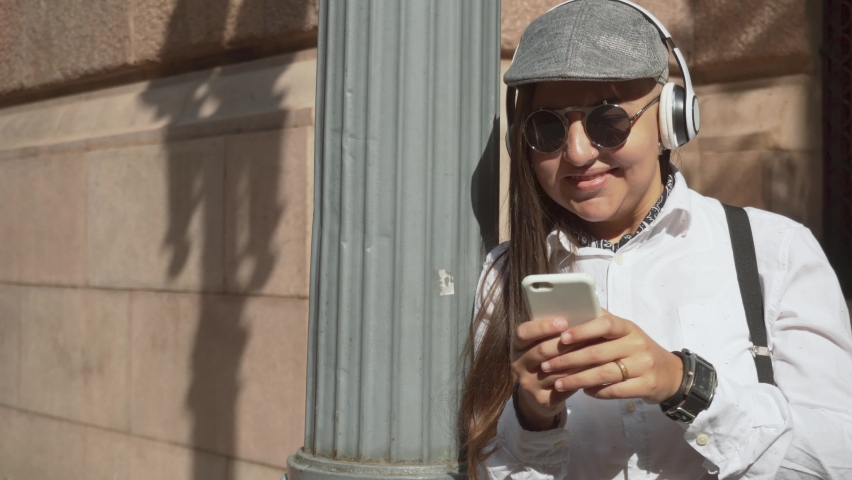 Portrait of chubby woman dressed in old fashion clothes listening to music and looking at mobile phone screen near old building. Weekend, joy, video, melody, energy, concept.