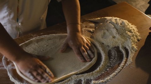 Cooking Italian pizza in a restaurant. Stretching raw pizza dough with your hands. A professional chef stretches and twists soft Italian pizza dough with his hands.