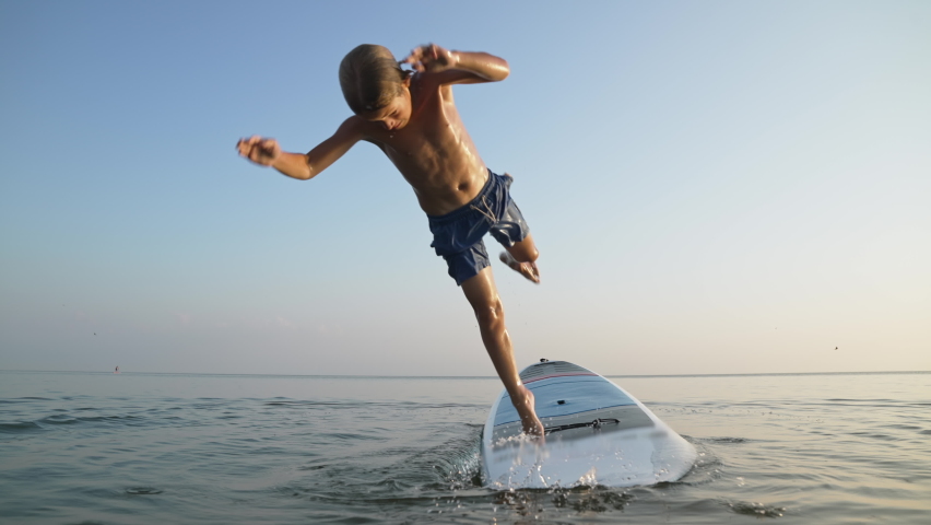 Happy child enjoying time in vacation on sea beach. Boy funny jumping to water from board on travel holiday at sunset. | Shutterstock HD Video #1077803993