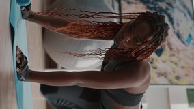 Verical video: Fit black woman in sportswear doing workout burning fat calories training strength practicing fitness on aerobic map in living room. Athlete adult enjoying healthy lifestyle practicing