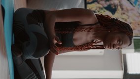 Verical video: Flexible black athlete relaxing in lotus position on floor in living room enjoying healthy lifestyles. Fitness woman in sportwear streching muscle during stretch gymnastics warming body