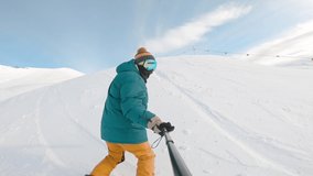 Concept of extreme, sport, winter, freeride, snowboarding. Man riding on snowboard with selfie stick in his hand downhill kamchatka mountain. Guy filming himself during riding down.