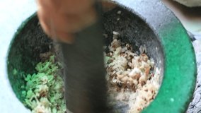 Gentleman’s hands hold stone granite pestle with mortar is grinding black pepper and herbs together with tropical herbs. Concept of cooking and gastronomy. Thai style cooking. 