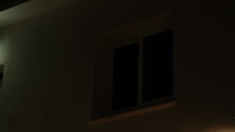 Light from the window of the house in the dark evening time. room lights up then turns off.