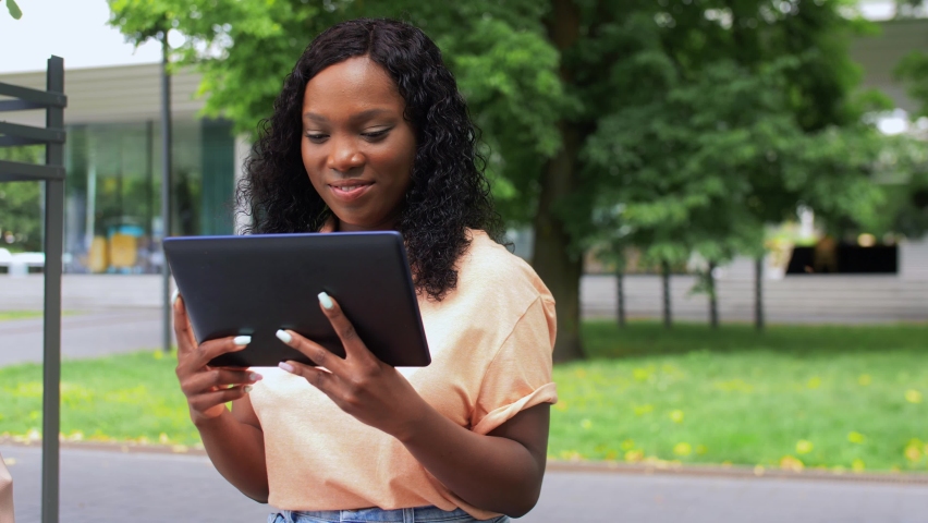 technology, education and people concept - happy smiling african american student girl with tablet pc computer taking notes in city