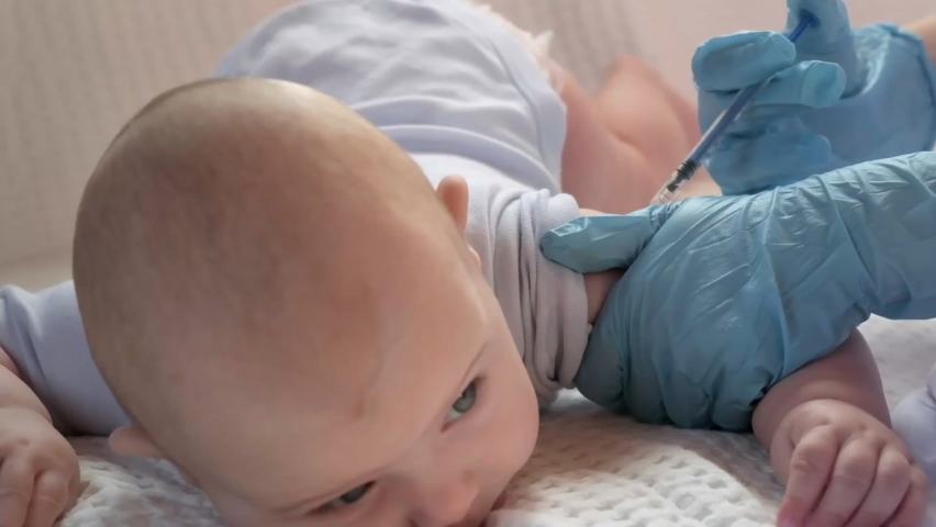 Pediatrician vaccinating newborn baby. Vaccine, Vaccination for infant child Soft focus Syringe in hands of nurse, blurred background of baby on white. Doctor in blue gloves close up. Mpox, Alaskapox Royalty-Free Stock Footage #1077815342