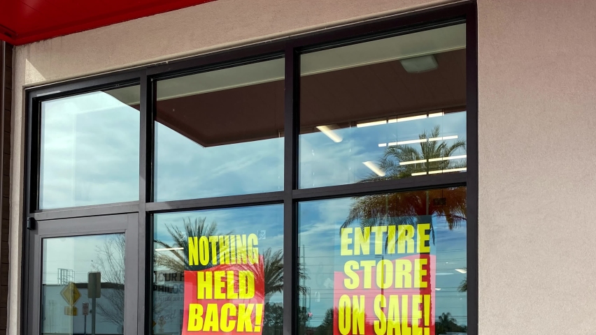 Panning down on signs in the window of a retail store going out of business that say the entire store on sale, everything must go and nothing held back.