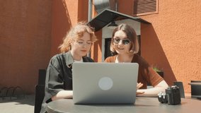 Young girls work remotely in a cafe on the summer terrace. Freelancers communicate with colleagues via video link.