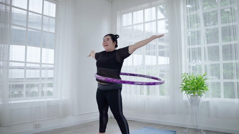 Fat Asian woman playing hula hoop to lose weight cheerfully in her room. health and weight loss concept
