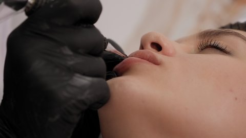 Cosmetologist applying permanent make-up on lips. Permanent makeup procedure in a modern beauty salon.