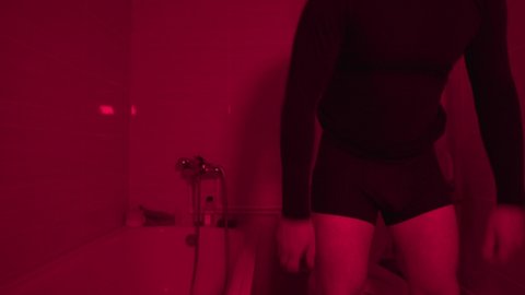 Young Man Dressing Pants after Toilet. Restroom in Red Light Lighted Room. A man in a Nightclub Toilet