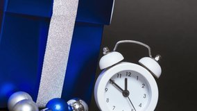 Christmas decorations. Composition with alarm clock, blue gift box and silver festive christmas balls on a black background.