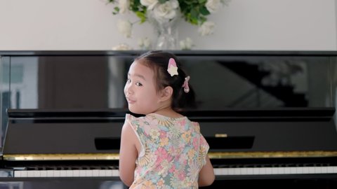 Asian girl playing piano in the back view of the camera. The girl turned around and looked at the camera after playing the piano.