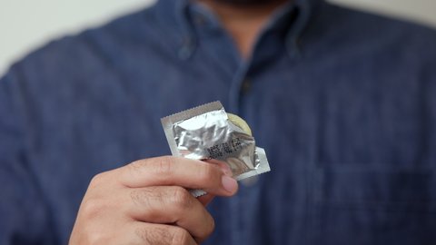 A young man unpacks a condom from a ready-to-use package. Campaign for safe sex and contraception.