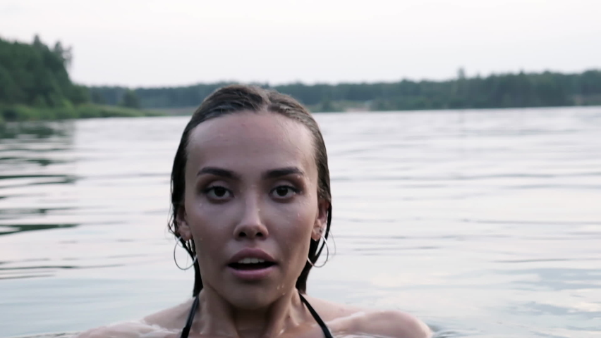 closeup on sexy seductive young woman who dives into lake, then pops up from water. attractive asian fit female with long hair in swimsuit swimming. summer chill, vacation, rest , fun, joy at nature