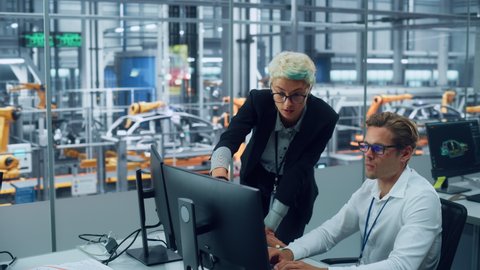 Two Automotive Engineers Discussing Concept Car Blueprints on Desktop Computer in Modern Office at Assembly Plant. Female Industrial Project Manager Talk to Male Designer at Vehicle Factory.