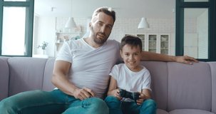 Middle aged man pointing on screen, excitedly sitting next to his son playing on virtual computer games. 4K video footage of Father and son spend time playing a computer game together